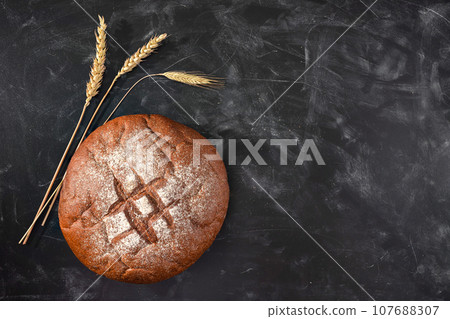 Loaf of fresh bread and wheat on a black table. Top view with copy space. Bakery concept 107688307