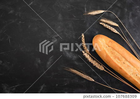Fresh french baguette and ears of wheat on a dark background. Top view with copy space. Bakery concept Fresh french baguette and ears of wheat on a dark background. Top view with copy space. Bakery concept 107688309