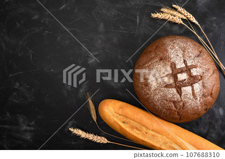 Fresh bread and grains of wheat on a dark background top view 107688310