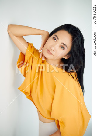Pretty sensual asian woman in bright yellow t-shirt posing on white studio background Pretty sensual asian woman in bright yellow t-shirt posing on white studio background 107689222