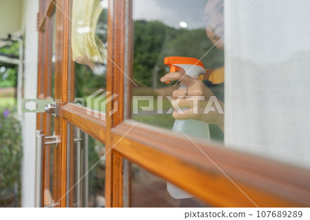 Young Asian housewife cleaning window glass with rags and detergent spray, cleaning house on the weekend 107689289