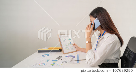 Happy young asian businesswoman talk on the mobile phone while sitting at working place in office 107689290