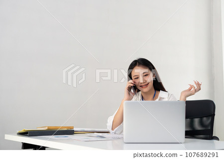 Happy young asian businesswoman talk on the mobile phone and smile while sitting at working place in office 107689291