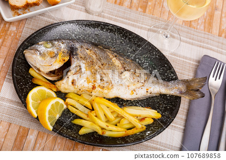 Baked dorada with french fries and fresh lemon slice 107689858