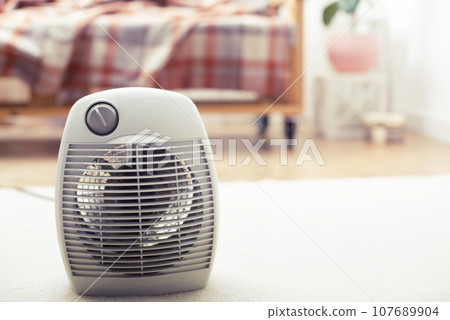 Fan heater on the floor in living room with sofa at background Fan heater on the floor in living room with sofa at background 107689904
