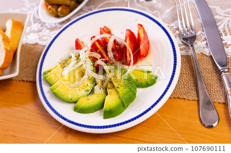 Pieces of avocado, tomato and onion rings served in a plate 107690111