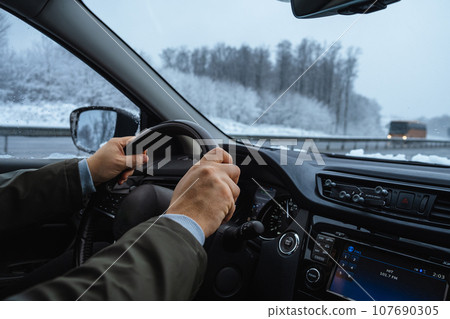 men's hands hold the steering wheel. winter road trip men's hands hold the steering wheel. winter road trip 107690305