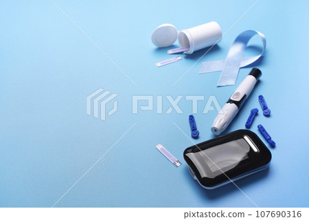 Diabetes awareness concept of ribbon glucose meter test strips and lancets on blue background 107690316