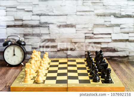 Chess pieces on chess board and alarm clock on wooden table. Blurred background with copy space 107692158