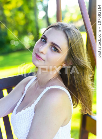 Belarus woman in white dress sitting on wooden swings Belarus woman in white dress sitting on wooden swings 107692164