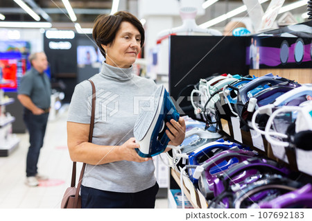 Elderly woman chooses iron in store 107692183