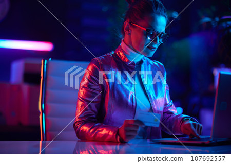trendy female in glasses with credit card using laptop trendy female in glasses with credit card using laptop 107692557