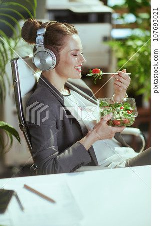 happy woman worker eating salad and listening to music 107693021
