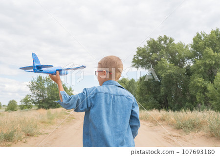 Rear view of a child boy with an airplane dreams of traveling in the summer in nature on a sunny day. 107693180