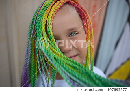 portrait of a little beautiful girl with multi-colored african braids on the background of a colorful wall 107693277