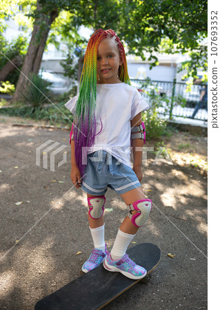little cute girl with colorful afro pigtails standing on a skateboard 107693352
