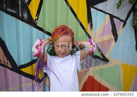 portrait of a little beautiful girl with multi-colored african braids on the background of a colorful wall portrait of a little beautiful girl with multi-colored african braids on the background of a colorful wall 107693393