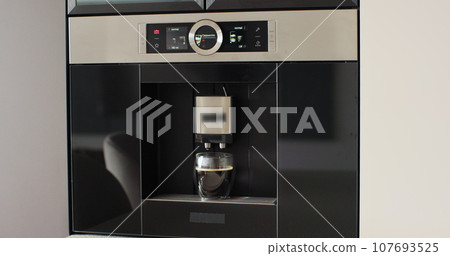 Automatic coffee machine pours coffee into mug in kitchen at home. Hot coffee drink concept. Automatic coffee machine pours coffee into mug in kitchen at home. Hot coffee drink concept. 107693525