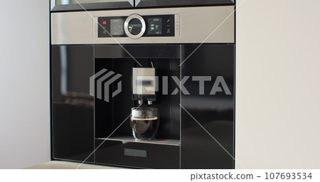 Automatic coffee machine pours coffee into mug in kitchen at home. Hot coffee drink concept. Automatic coffee machine pours coffee into mug in kitchen at home. Hot coffee drink concept. 107693534