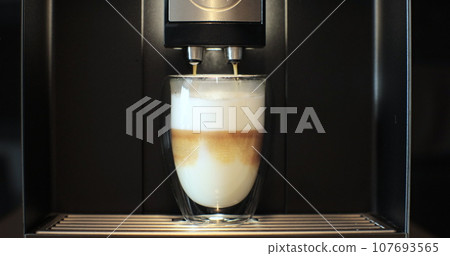 Close-up of coffee being poured into a glass cup with milk, making cappuccino with an automatic coffee machine. Close-up of coffee being poured into a glass cup with milk, making cappuccino with an automatic coffee machine. 107693565