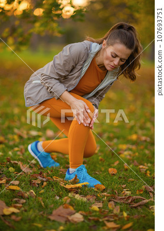 sad modern woman in fitness clothes in park got leg injury 107693751