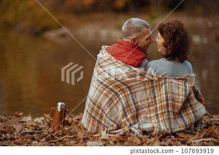 Seen from behind modern couple in park with blanket hugging Seen from behind modern couple in park with blanket hugging 107693919