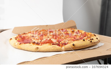 Italian Pizza in Cardboard Delivery Box, Ham Pizza with Green Hot Pepper, Chili Pepper and Mozzarella Cheese Italian Pizza in Cardboard Delivery Box, Ham Pizza with Green Hot Pepper, Chili Pepper and Mozzarella Cheese 107694324