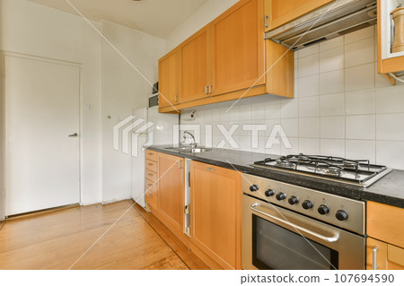 a kitchen with wood cabinets and an oven in the middle part of the room on the right is a white wall 107694590
