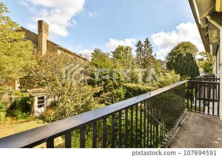 a balcony with trees and buildings in the background, taken from an apartment window looking out to the street below 107694591