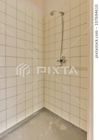 a shower stall with white tiles on the walls and floor in an empty room, it appears to be used as a bathroom 107694610