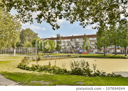 an empty park in the middle of a residential area, with trees and grass growing on either side of the road 107694844