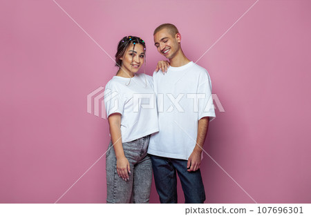 Attractive young woman and man wearing white empty t-shirt on bright pink studio wall background 107696301