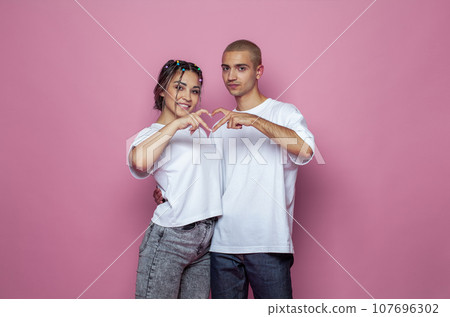 Young adult woman and man in white empty t-shirt standing on bright pink studio wall background 107696302