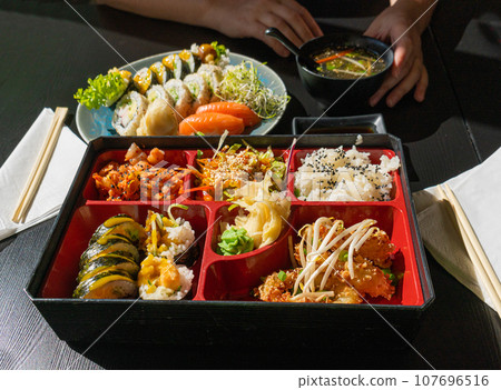 Japanese Lunch in Bento Box with Deep-Fried Squid Rings, Sushi Rolls, Salad, Rice, Pickled Ginger Japanese Lunch in Bento Box with Deep-Fried Squid Rings, Sushi Rolls, Salad, Rice, Pickled Ginger 107696516