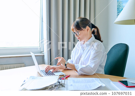 Mature business woman working at desk in home office, using laptop 107697031