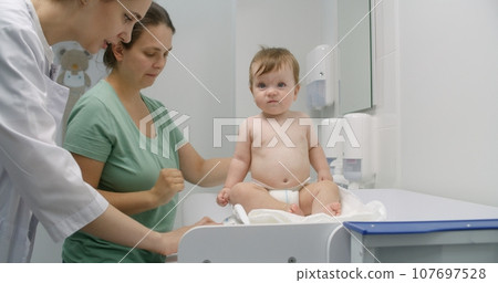 Female doctor weighs kid in modern hospital room 107697528