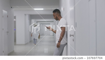 African American man stands in hospital corridor and chats by phone 107697704