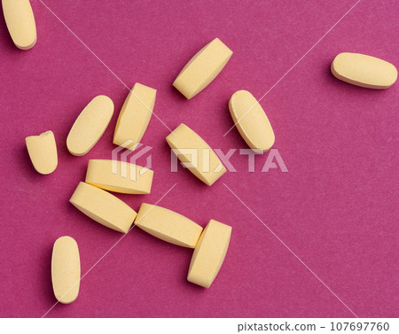 Yellow oval tablets on a pink background, top view 107697760