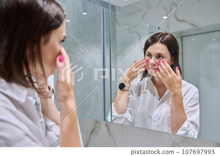 Young woman looking at her face in bathroom mirror 107697993