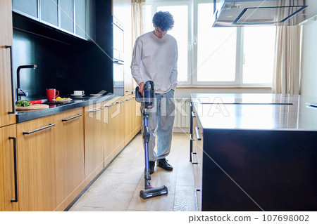 Young guy doing vacuuming at home 107698002
