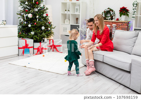 A family of three celebrates Christmas with a Christmas tree under which there are gifts 107698159