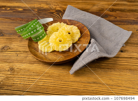 Dry Pineapple Rings on Wood Plate, Candy Pineapples, Dehydrated Yellow Sugar Fruit, Candied Fruits Circles Dry Pineapple Rings on Wood Plate, Candy Pineapples, Dehydrated Yellow Sugar Fruit, Candied Fruits Circles 107698494