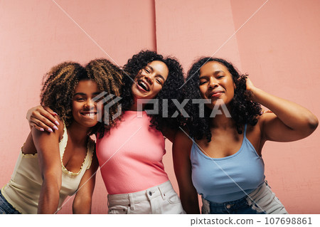 Three happy girls with curly hair standing together and looking at camera	 107698861