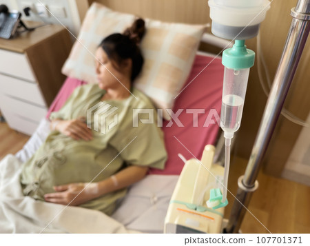 medical saline IV drip with pregnant woman resting on a bed in hospital 107701371