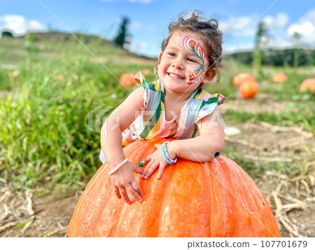 Little girl picking pumpkins on Halloween pumpkin patch. Child playing in field of squash. 107701679