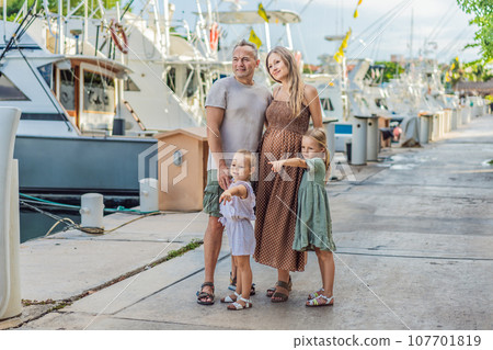 A happy, mature couple over 40 with their two daughters enjoying a leisurely walk on the waterfront, their joy evident as they embrace the journey of pregnancy later in life A happy, mature couple over 40 with their two daughters enjoying a leisurely walk on the waterfront, their joy evident as they embrace the journey of pregnancy later in life 107701819