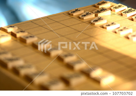 Shogi pieces lined up on a shogi board in bright light 107703702