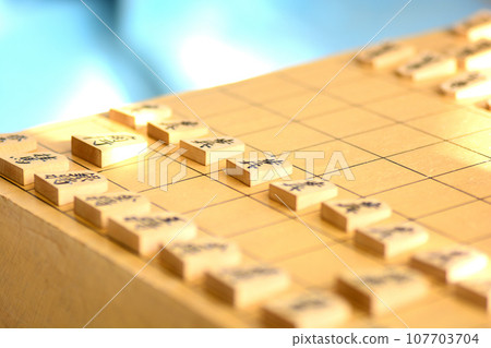 Shogi pieces lined up on a shogi board in bright light 107703704