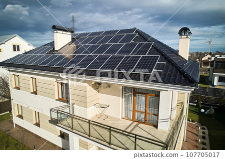 Home residence with solar panel system for generating electricity through photovoltaic effect. Aerial view of two-storey house with solar modules on roof. Ecological renewable energy sources concept. 107705017
