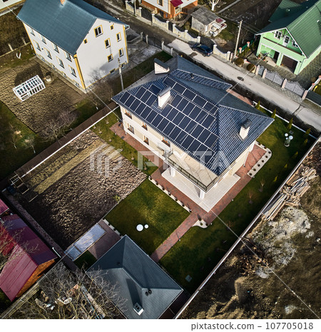 Aerial view of modern residential house with photovoltaic solar panels on roof. House with yard, residential buildings and homes with solar electric system in new suburban district. 107705018